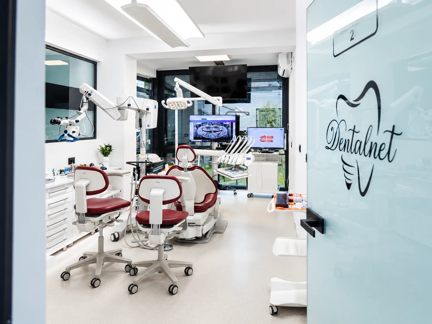 Cabinet DentalNet cu scaune roșii și ecrane cu radiografii, ușa cu logo-ul clinicii